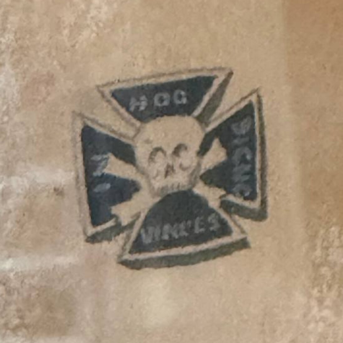 Close detail of the small cross-shaped pin in the sitter's shirt front: a black Maltese cross with a skull and crossbones at the centre